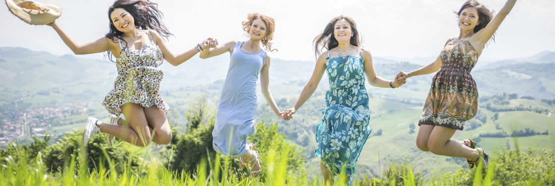 Four women holding hands and jumping in the summer sunshine