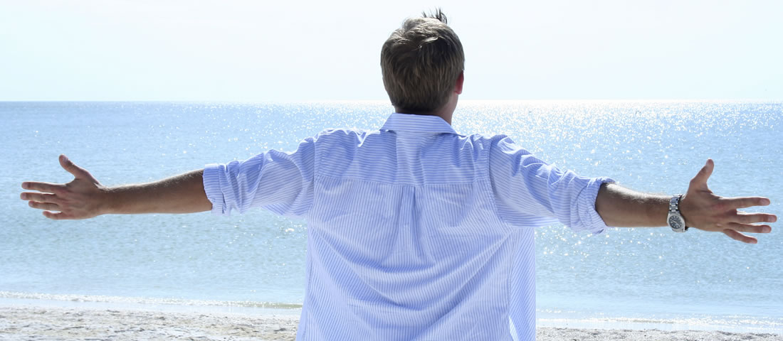 A man facing the ocean with his hands raised to the side