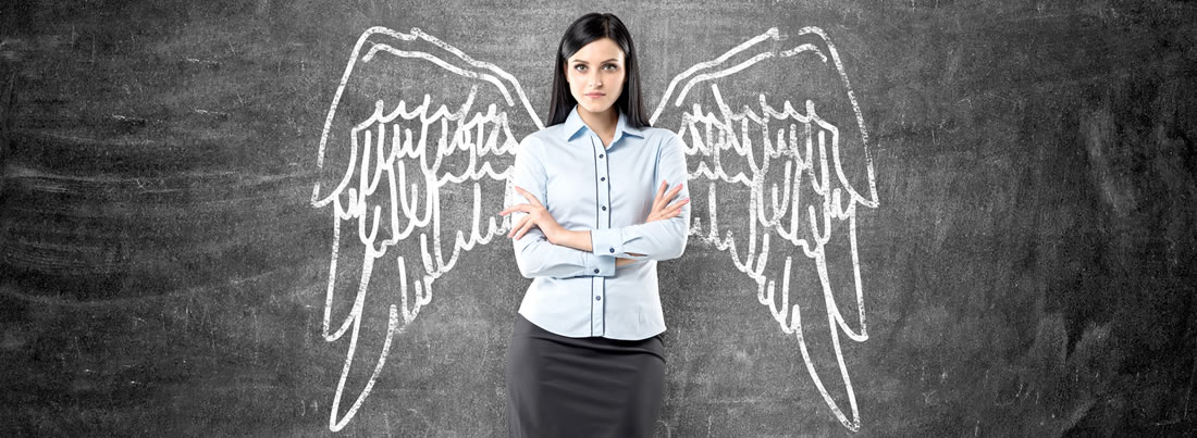 A woman standing in front of a chalkboard with wings drawn behind her.