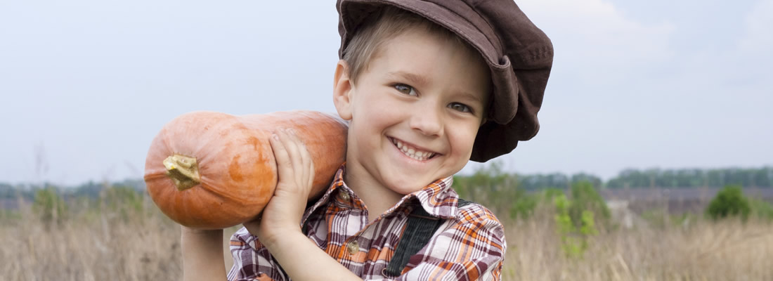 A young boy holding a squash in the fall wearing overalls